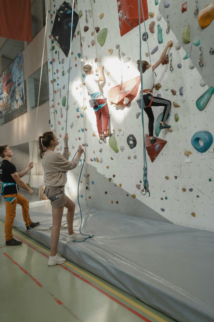 Group of people engaged in indoor rock climbing with harnesses and ropes.